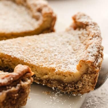 A slice of pie dusted with powdered sugar is lifted by a pie server.