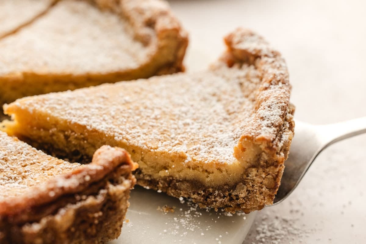 A slice of pie dusted with powdered sugar is lifted by a pie server.