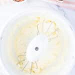A mixing bowl with electric mixer beaters and creamy batter, next to a bowl of rainbow sprinkles and cracked eggshells on a striped cloth.