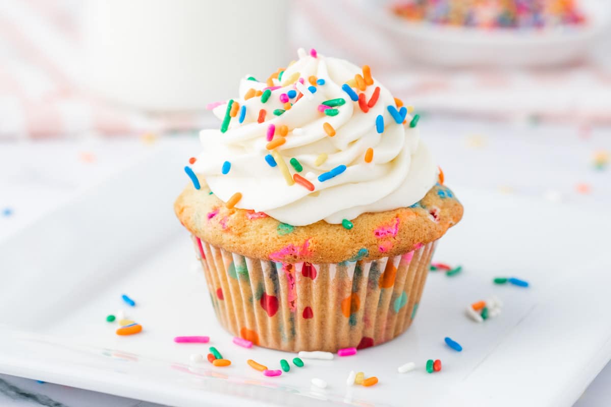 Funfetti cupcakes with rainbow sprinkles, topped with whipped cream–cream cheese frosting.