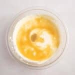 A glass bowl containing a mixture of cream and honey on a light-colored surface.