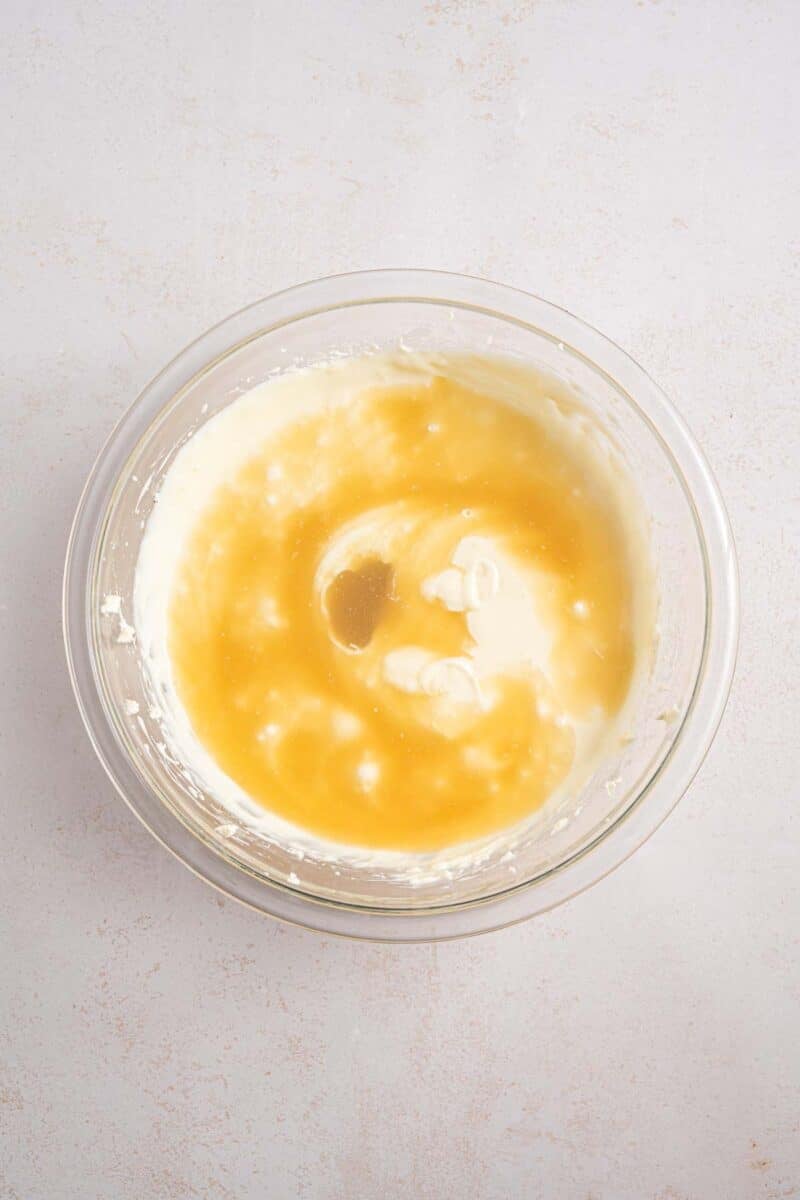 A glass bowl containing a mixture of cream and honey on a light-colored surface.