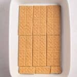 Rectangular graham crackers are neatly arranged in a single layer at the bottom of a white rectangular baking dish.