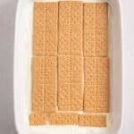 Rectangular baking dish with a layer of graham crackers on top of a white creamy base, placed on a light-colored surface.