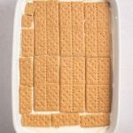 Rectangular baking dish with a layer of whole and broken graham crackers placed over a creamy white filling.