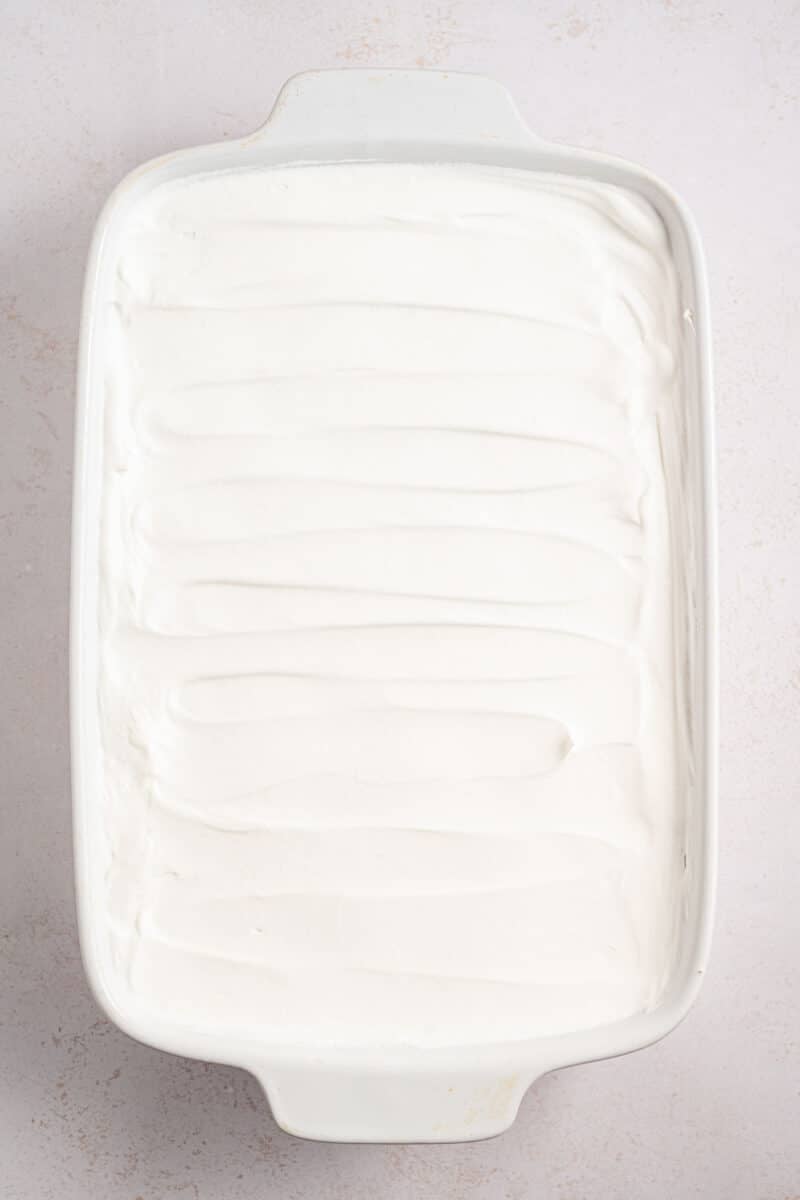A rectangular white baking dish filled with a smooth, evenly spread layer of white whipped topping.
