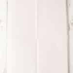 A square baking sheet lined with a large piece of white parchment paper on a rustic white wooden surface.