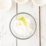 A glass bowl with powdered sugar and lime zest on a white wooden surface, with three empty small bowls above it.
