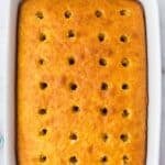 A rectangular baked cake in a white dish with evenly spaced holes poked into the surface.