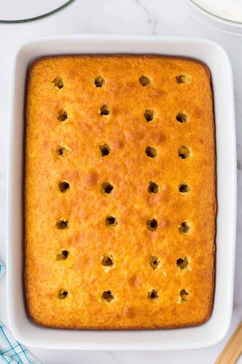 A rectangular baked cake in a white dish with evenly spaced holes poked into the surface.