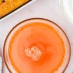 A bowl of orange gelatin mixture on a marble surface next to a partially visible poked cake and a bowl of whipped topping.