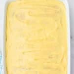 A rectangular baking dish filled with a smooth layer of yellow pudding mixture on top, placed on a marble surface.