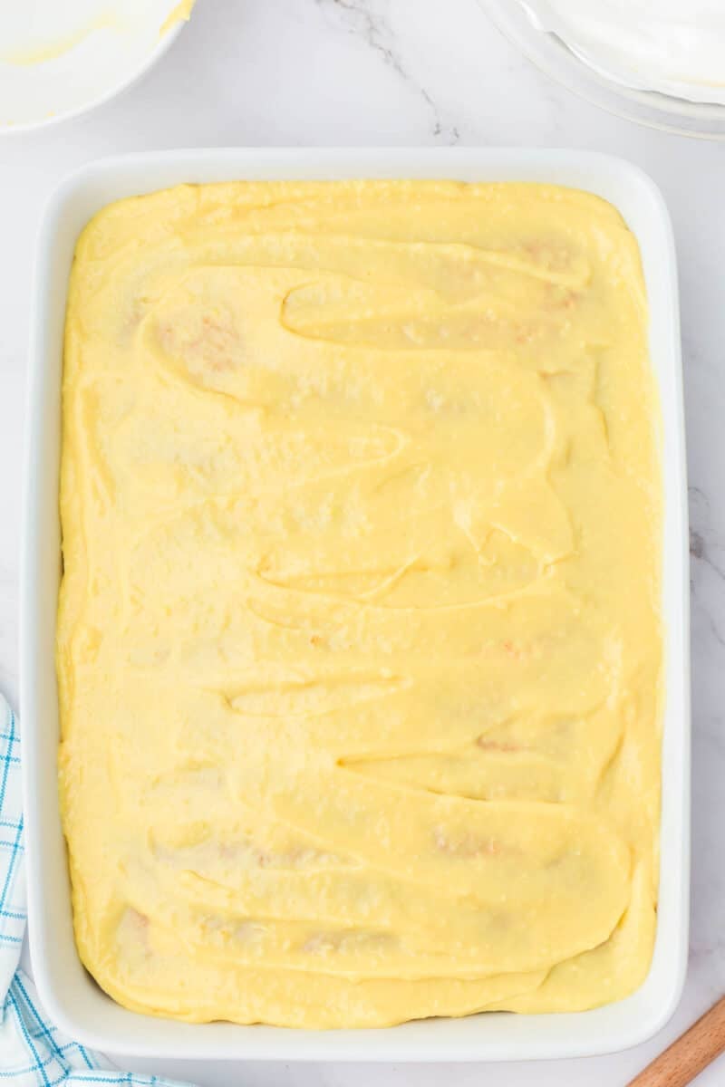 A rectangular baking dish filled with a smooth layer of yellow pudding mixture on top, placed on a marble surface.