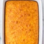 A rectangular, golden-brown baked cake in a white ceramic dish on a marble surface.
