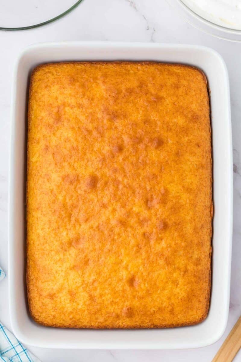 A rectangular, golden-brown baked cake in a white ceramic dish on a marble surface.