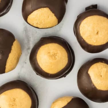 A group of round peanut butter balls partially dipped in chocolate, arranged on a light surface.