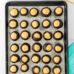 A tray of buckeye candies with peanut butter centers partially dipped in chocolate, arranged in rows on parchment paper.