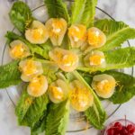 A plate of romaine lettuce topped with sliced pears, dollops of mayonnaise, and shredded cheddar cheese, with a bowl of maraschino cherries on the side.
