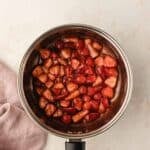 Chopped strawberries in syrup in a stainless steel saucepan.