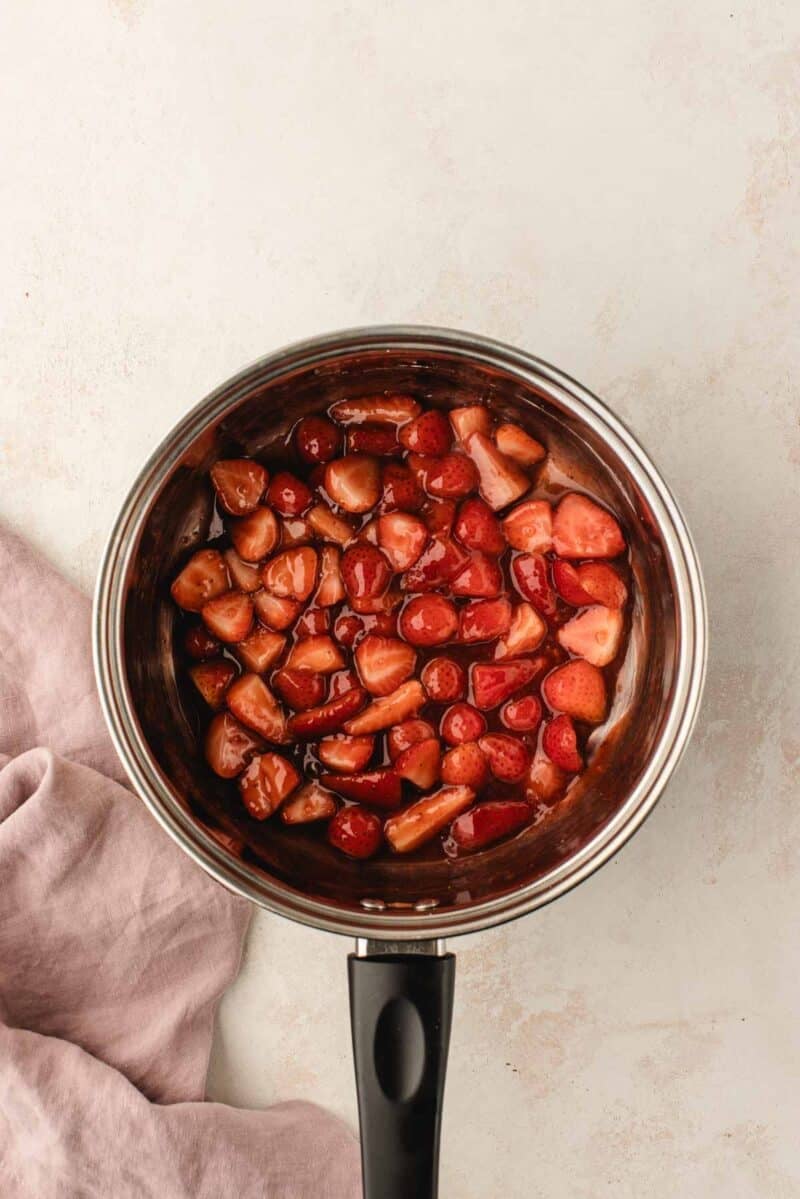 Chopped strawberries in syrup in a stainless steel saucepan.