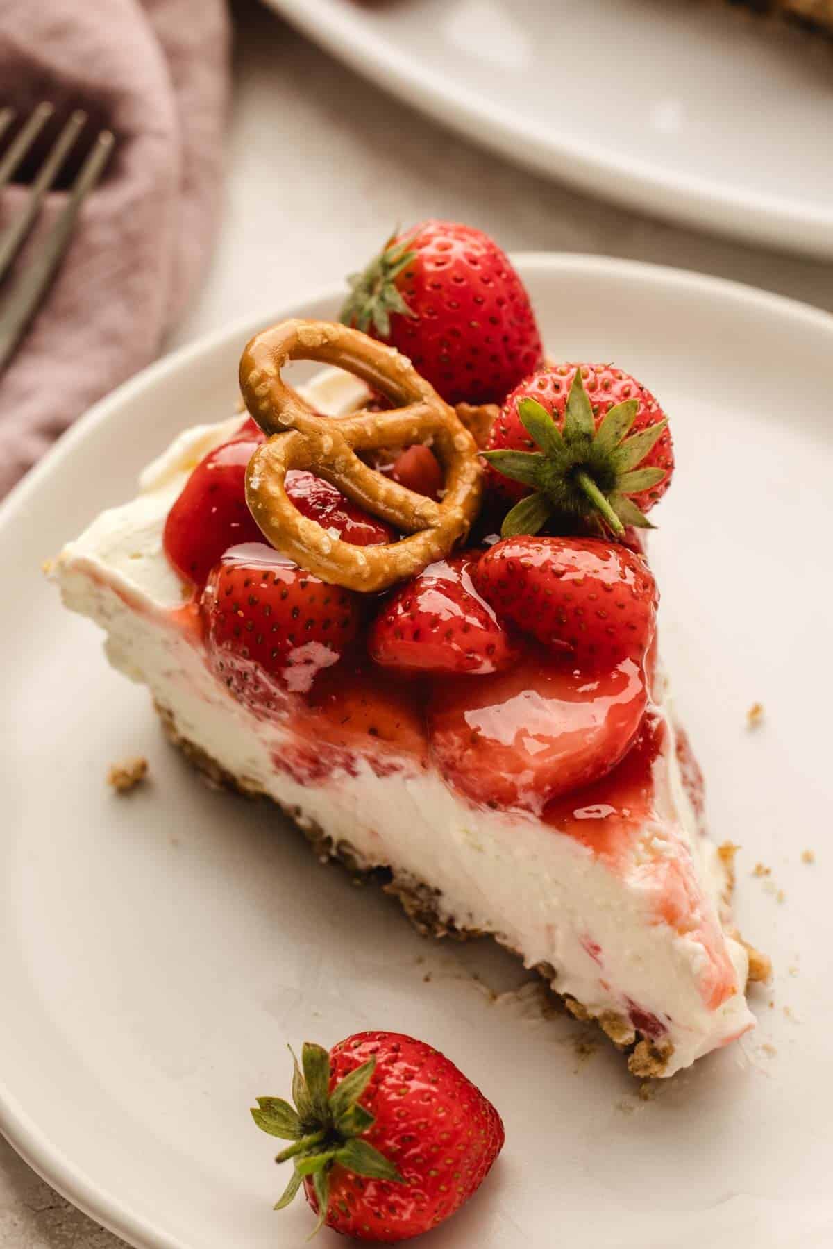 Slice of strawberry pretzel pie topped with fresh strawberries and a pretzel.