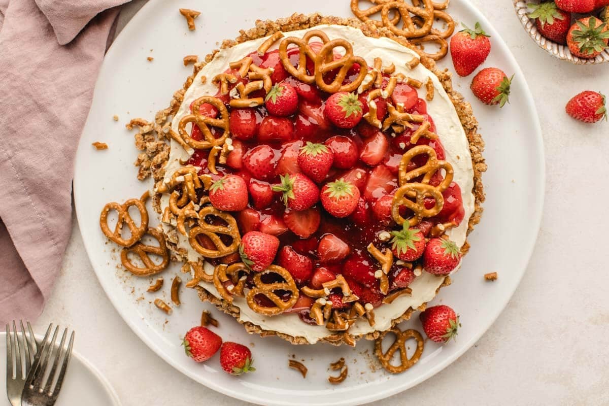 A strawberry pretzel tart topped with cream cheese, jam, and pretzels.