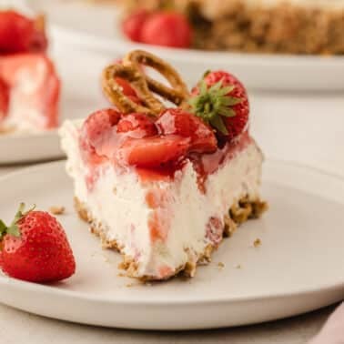A slice of strawberry pretzel pie on a white plate, topped with strawberries and pretzels.