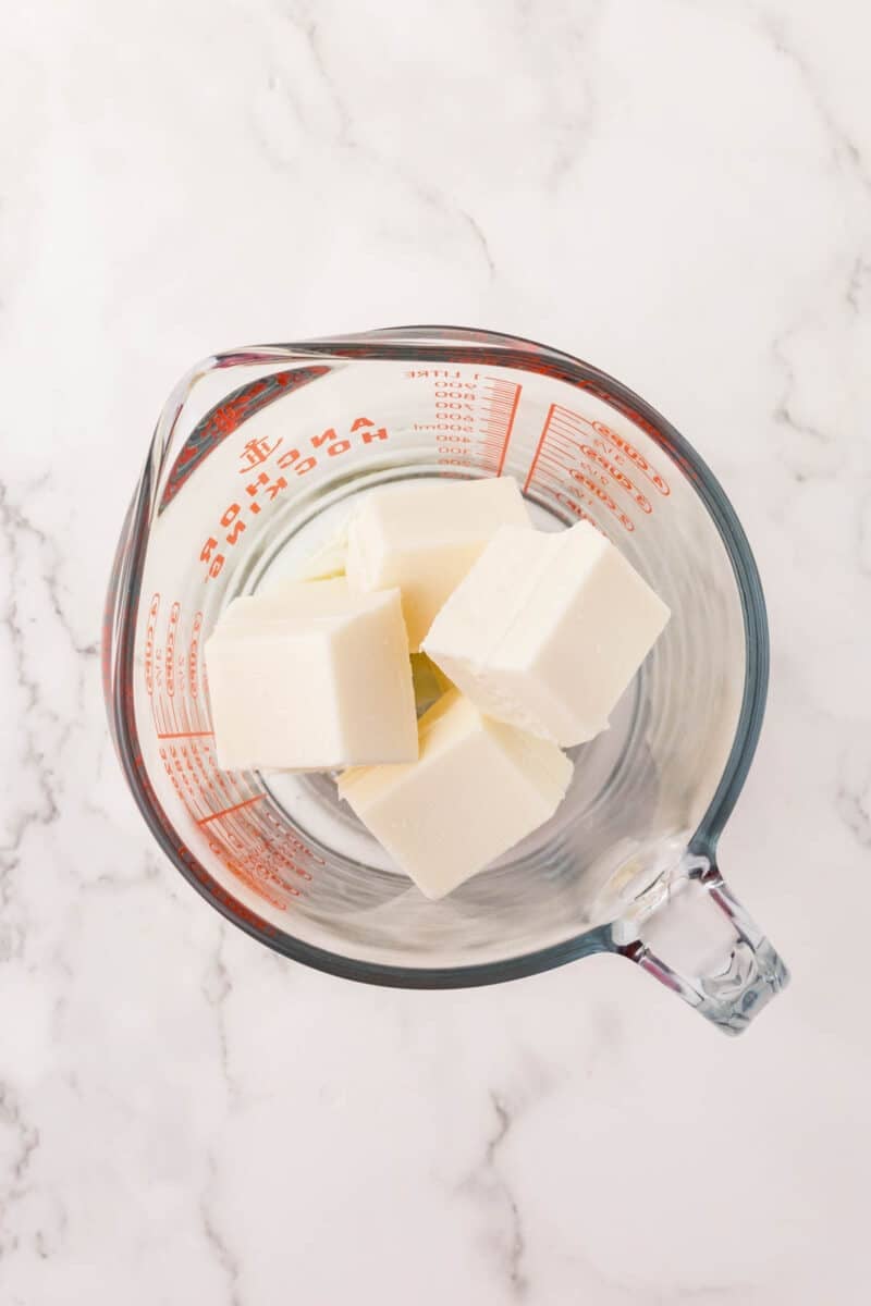 Glass measuring cup with several rectangular blocks of white butter or shortening on a white marble surface.