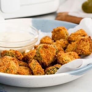 A plate of breaded, golden-brown fried pickles is served with a small bowl of dipping sauce on the side.