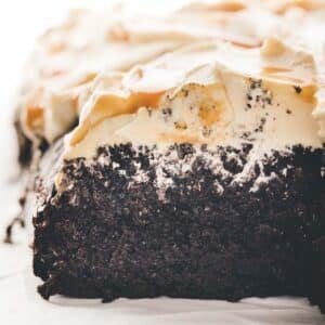 A close-up of a chocolate cake with a thick layer of whipped cream and caramel sauce on top, shown in cross-section.