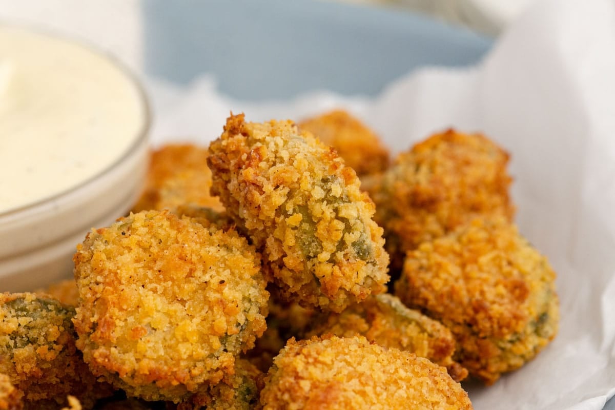 A close-up of air fryer fried pickles served on parchment paper with a bowl of dipping sauce in the background.