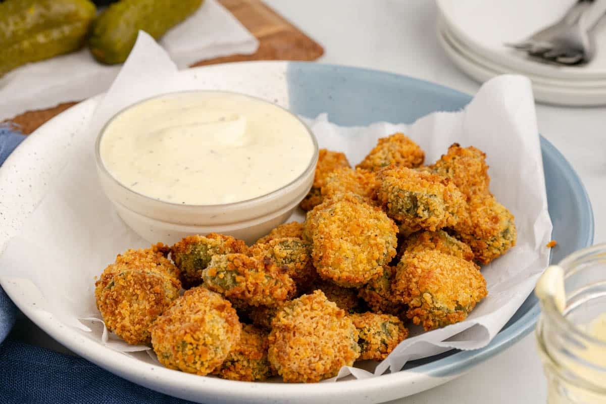A plate of air fryer fried pickles is served with a bowl of white dipping sauce on parchment paper.