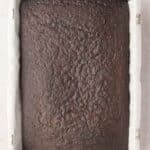 A rectangular pan lined with parchment paper holds a freshly baked, uncut chocolate cake.