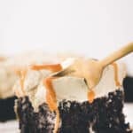 A slice of chocolate cake with caramel drizzle and whipped topping on a plate, with a fork inserted into the cake.
