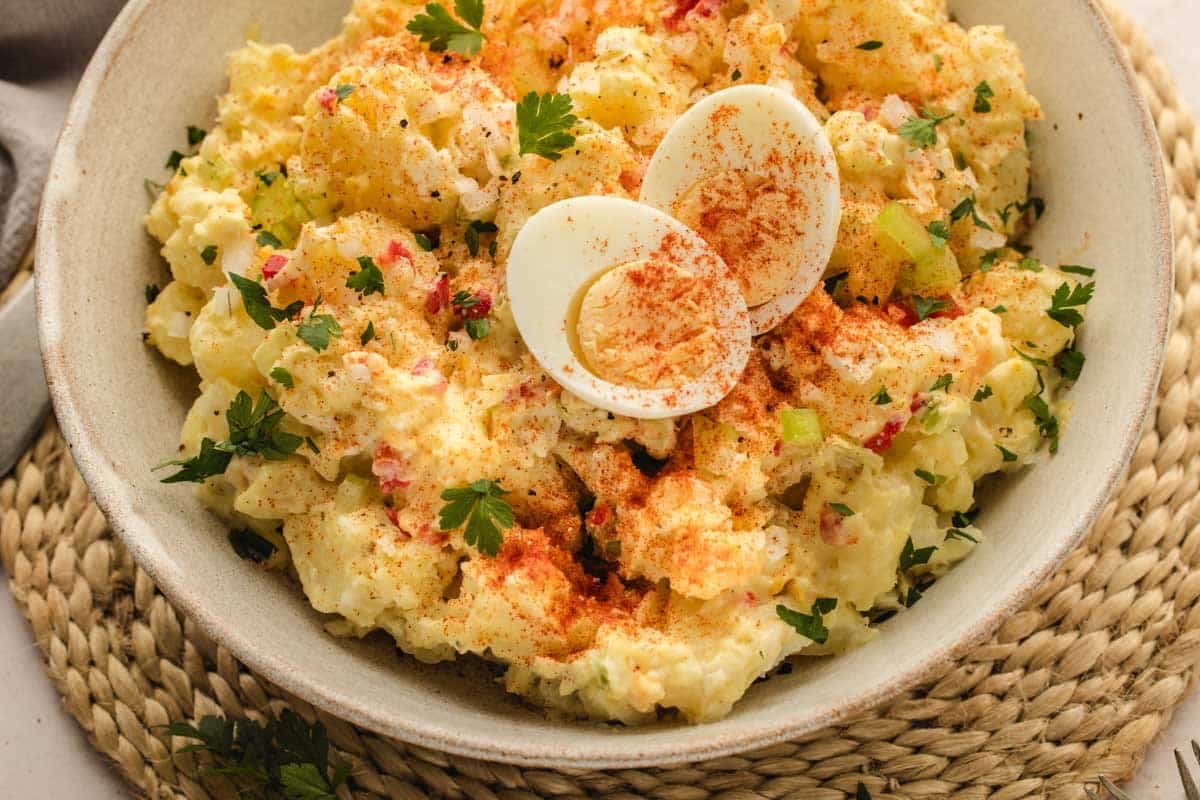 A bowl of potato salad topped with sliced hard-boiled egg halves, parsley, and paprika, served on a woven placemat.