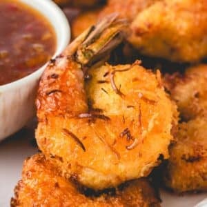 Close-up of air fryer coconut shrimp on a plate next to a small bowl of dipping sauce.