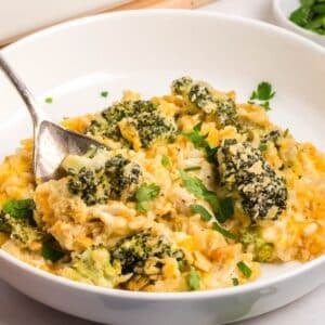 A white bowl with chicken broccoli rice casserole topped with breadcrumbs and chopped parsley, with a spoon resting in the dish.