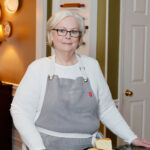 Lana Stuart, of Lanascooking.com, standing in her kitchen in a grey apron.