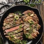 Sliced ribeye steak with herbs and garlic in a cast iron skillet, photographed from above on a rustic surface.