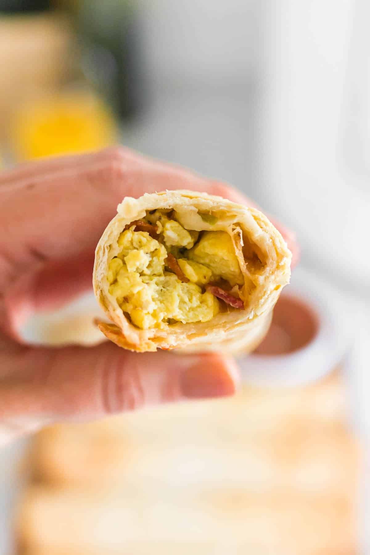 A hand holds a half-eaten air fryer breakfast taquito, showing scrambled eggs and bacon inside a tortilla.