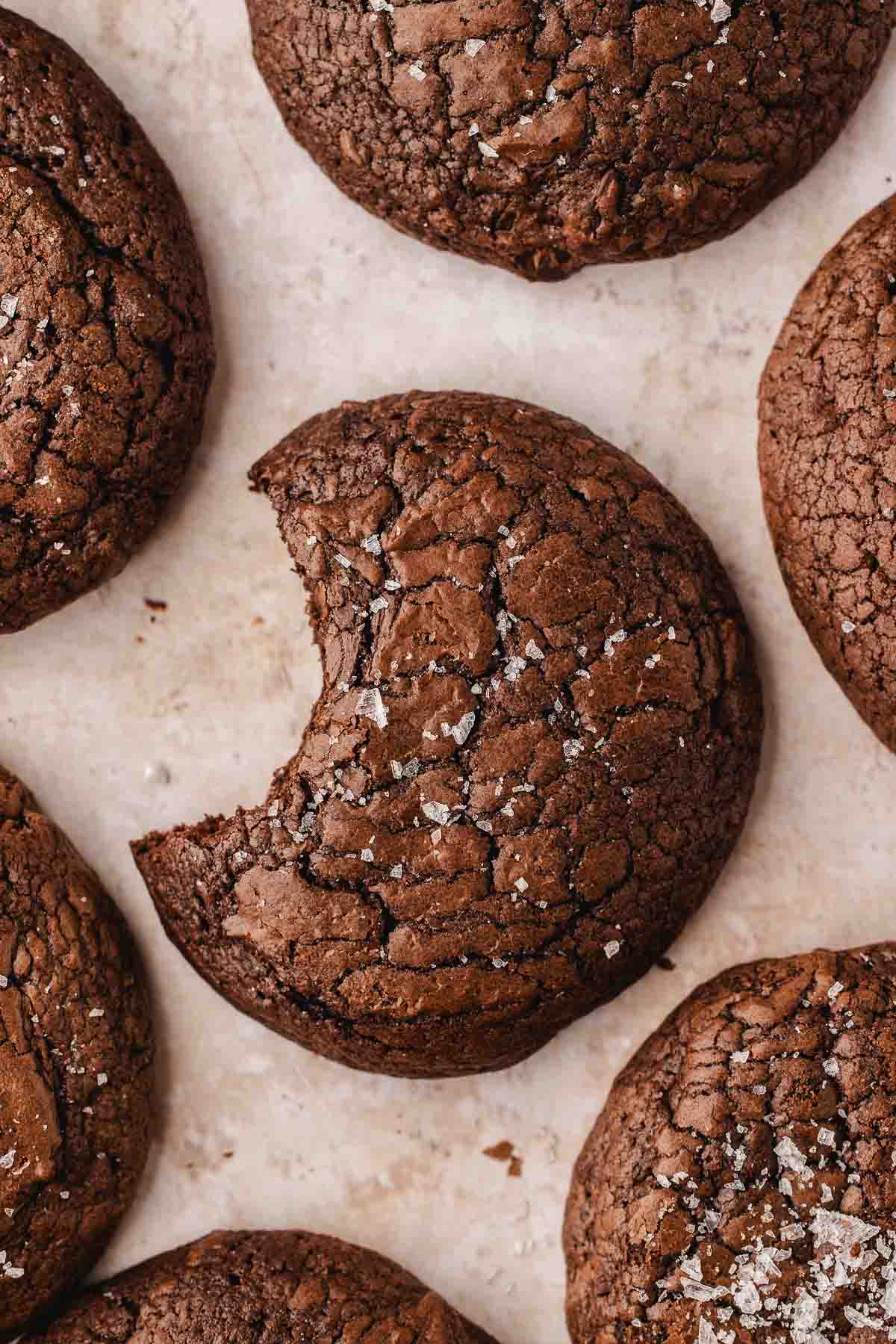 A close-up of several brownie cookies on a light surface, with one cookie showing a large bite taken out of it.