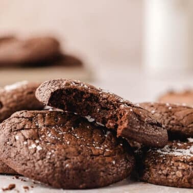 A close-up of brownie cookies stacked on a surface, with one cookie showing a bite taken out.