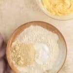A bowl with flour, almond flour, baking powder, and salt next to a bowl of creamed butter and sugar on a textured surface.