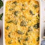 A baked casserole in a white dish, featuring chicken broccoli rice casserole, and a golden cracker topping, surrounded by parsley and crackers on a light surface.