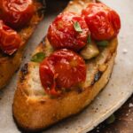 Grilled bread topped with tomato confit and fresh herbs on a ceramic plate.