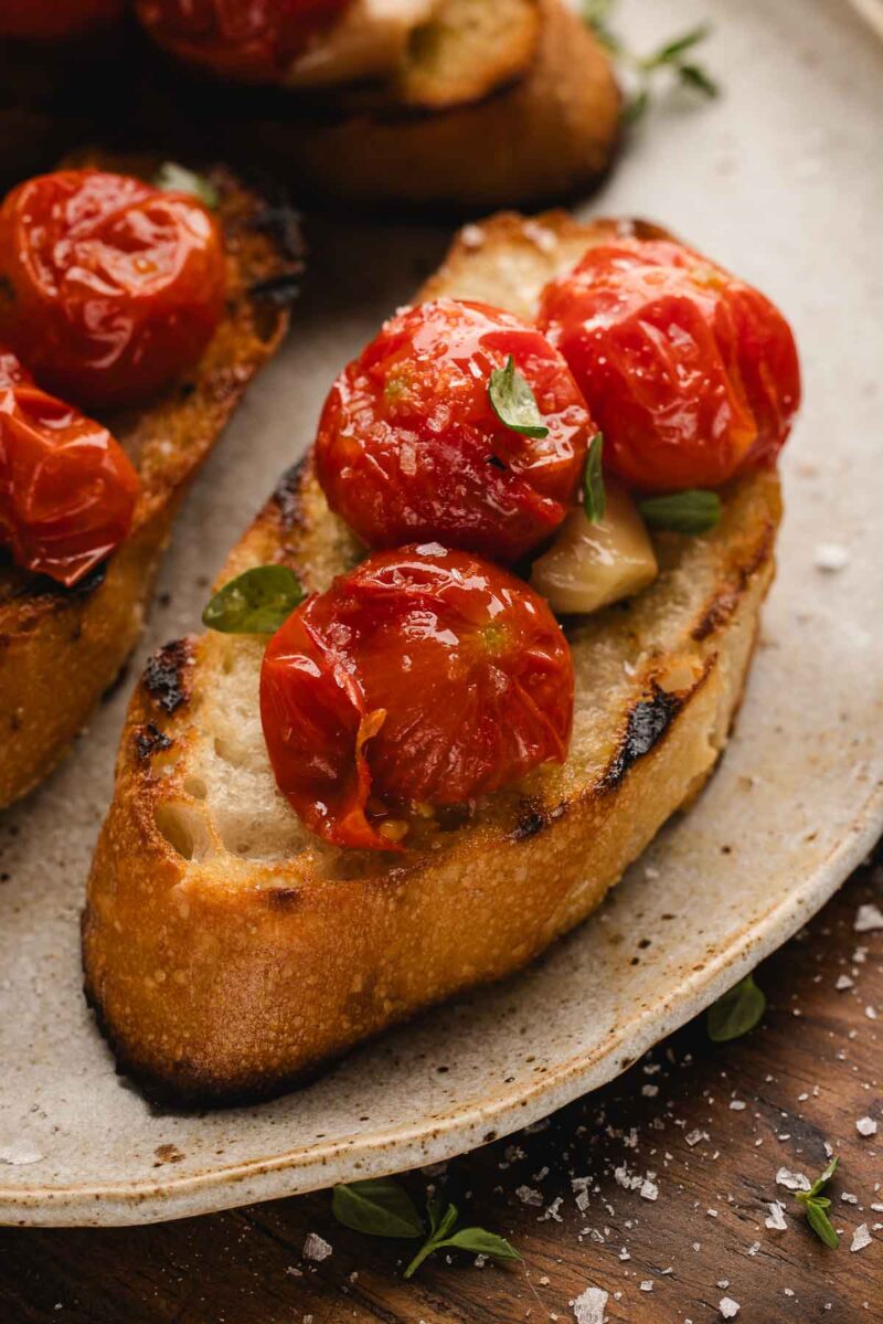 Grilled bread topped with tomato confit and fresh herbs on a ceramic plate.