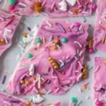 Broken pieces of Unicorn bark topped with colorful sprinkles and small candy decorations on a light surface.