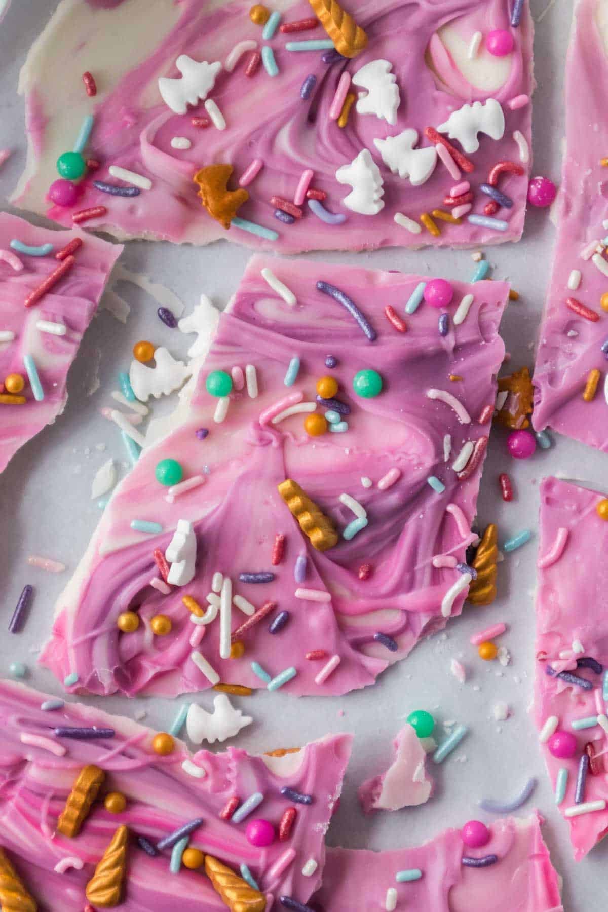 Broken pieces of Unicorn bark topped with colorful sprinkles and small candy decorations on a light surface.