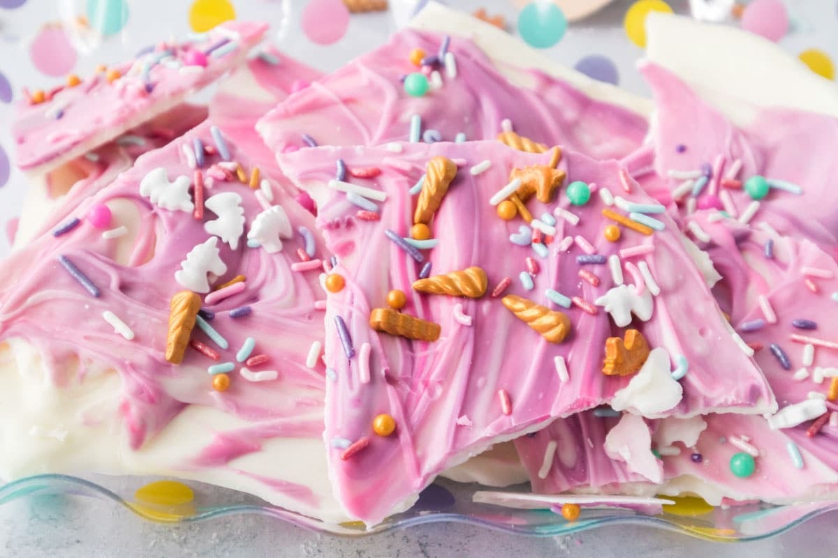 Unicorn bark topped with colorful sprinkles and candy shapes, arranged on a glass plate.