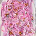 Unicorn bark topped with colorful sprinkles, mini pretzel pieces, and small candy shapes on a flat surface.